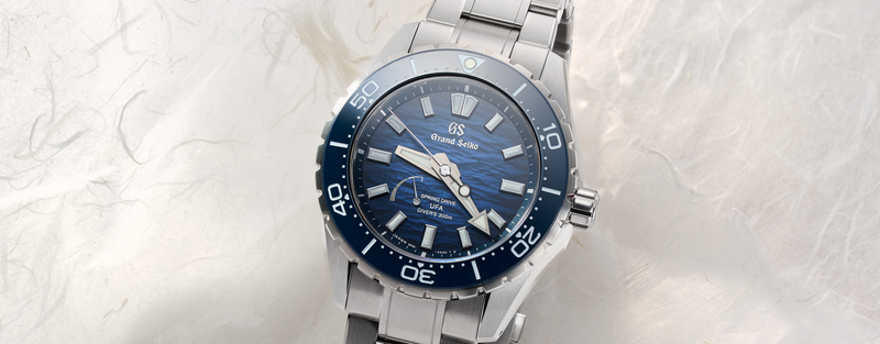 Grand Seiko diver watch with blue dial and metal bracelet on a light marble background.