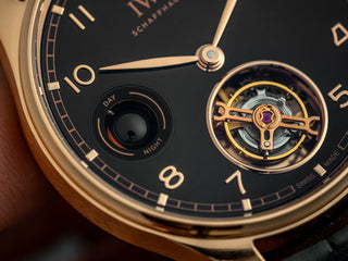 Close-up of a black dial luxury watch with gold hands and a visible tourbillon.