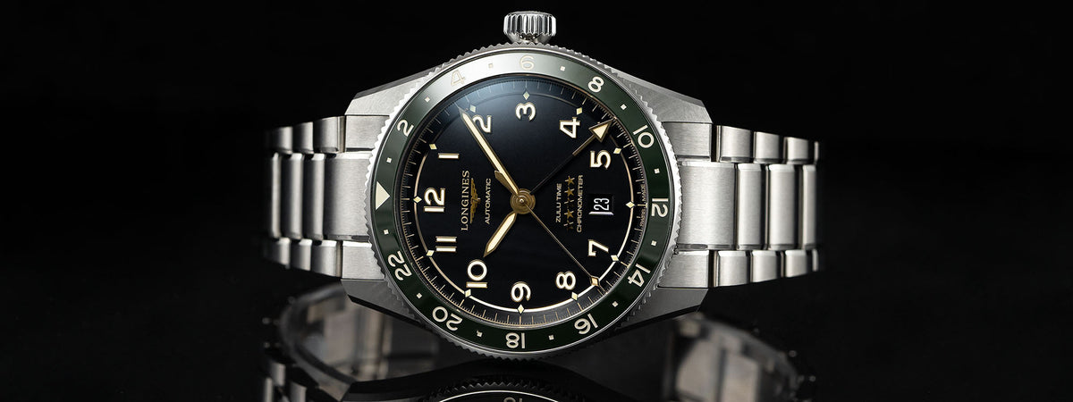 Longines automatic watch with black dial and green bezel on a stainless steel bracelet.