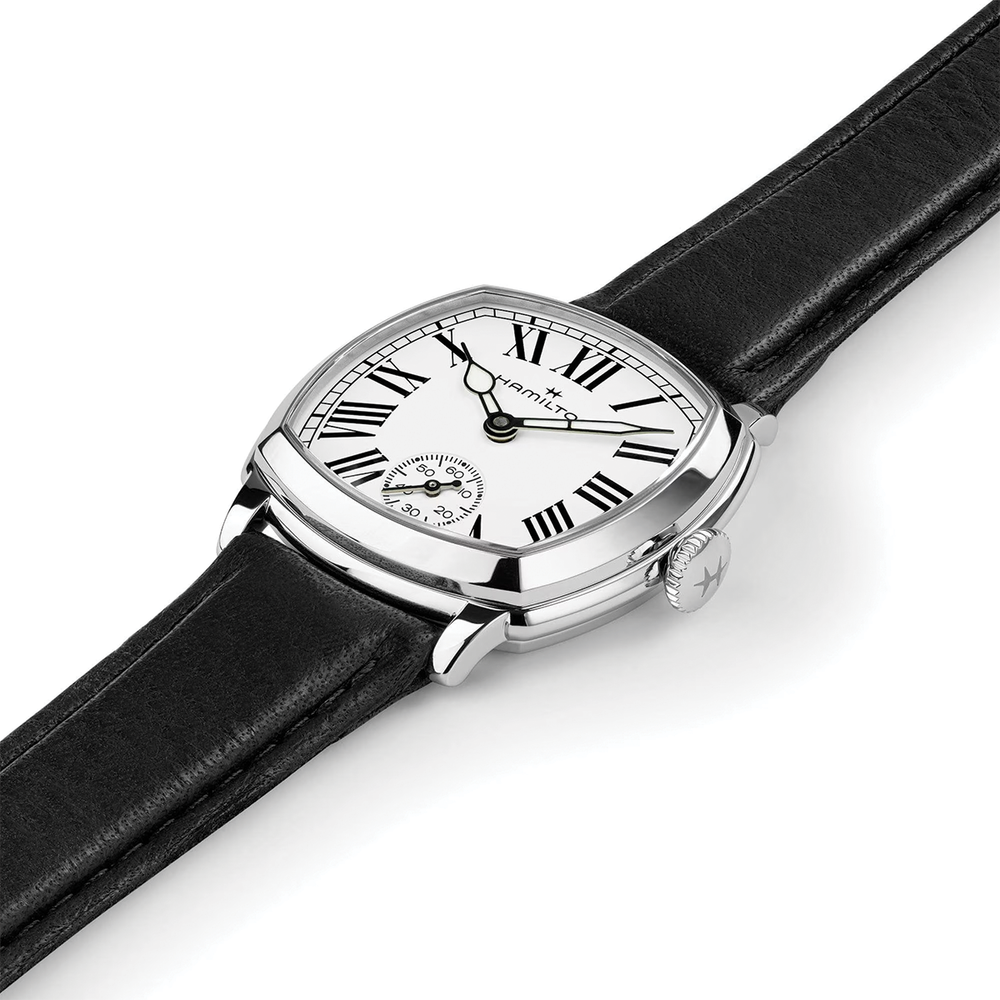 Close-up of cushion shaped watch with white dial Roman numerals on black leather strap.