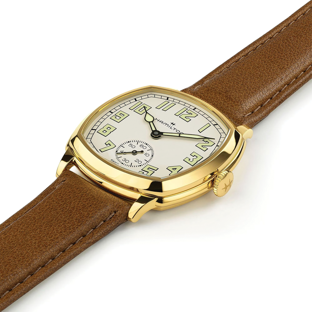 Angled view of gold tone cushion watch with beige dial and brown leather strap