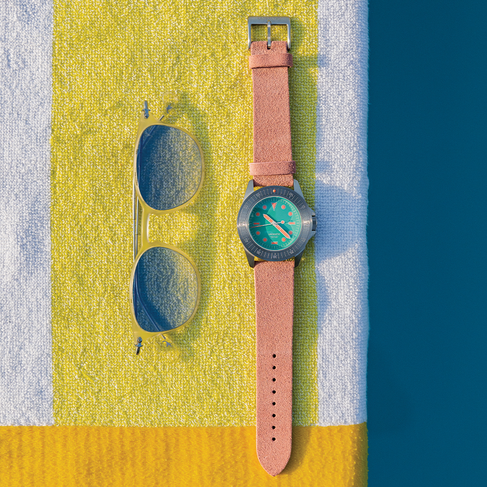 Turquoise dial watch with pink leather strap resting on a colorful towel beside sunglasses