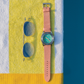 Turquoise dial watch with pink leather strap resting on a colorful towel beside sunglasses