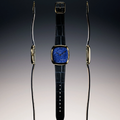 Center front gold square watch with blue lapis lazuli dial on a blue leather strap flanked by side views of the case.