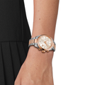 Wrist wearing a two-tone Tissot PR 100 chronograph with a rose gold and stainless steel bracelet and a white mother-of-pearl dial