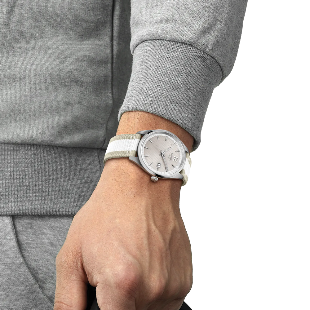 Wrist shot of Tissot PR 100 quartz watch with beige white striped fabric strap on a gray sleeve