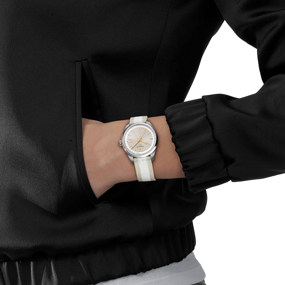 Wrist shot of a Tissot PR 100 34mm watch with grey dial and beige white striped fabric strap.