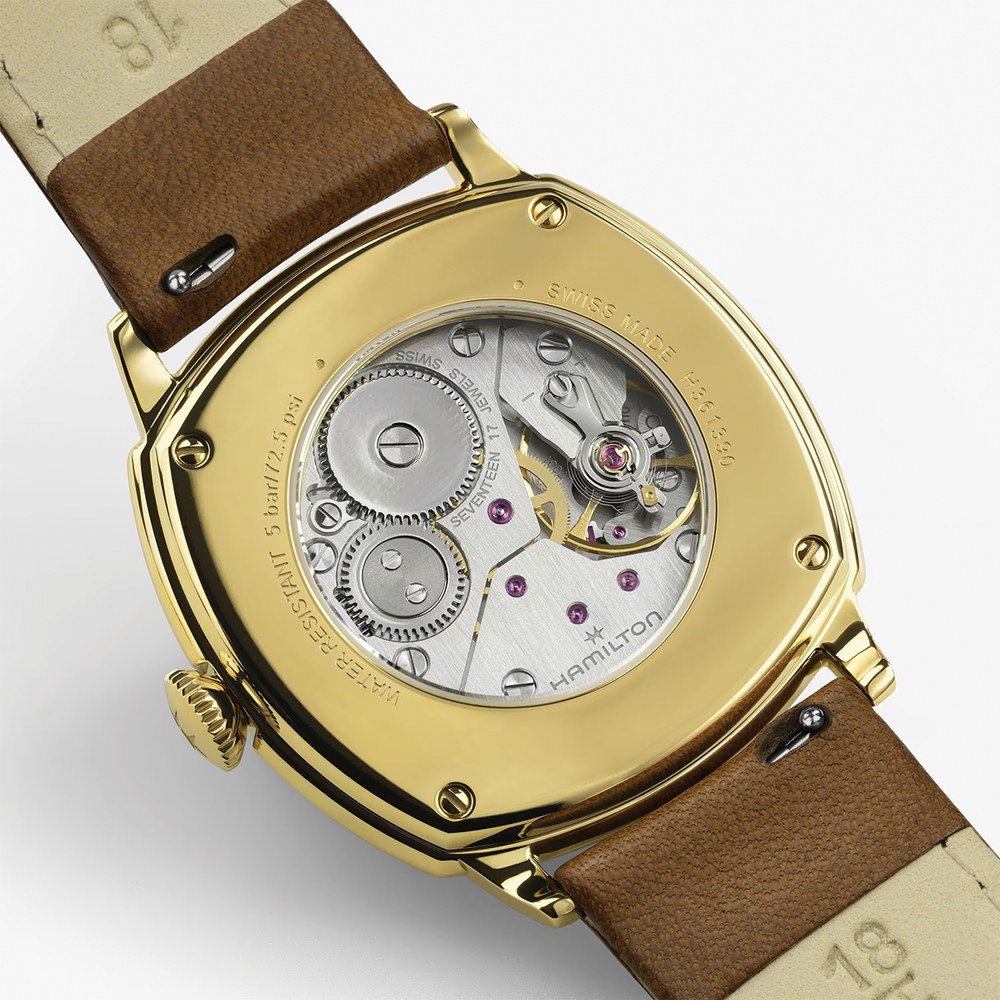 Gold-tone cushion watch back with brown leather strap showing exposed movement