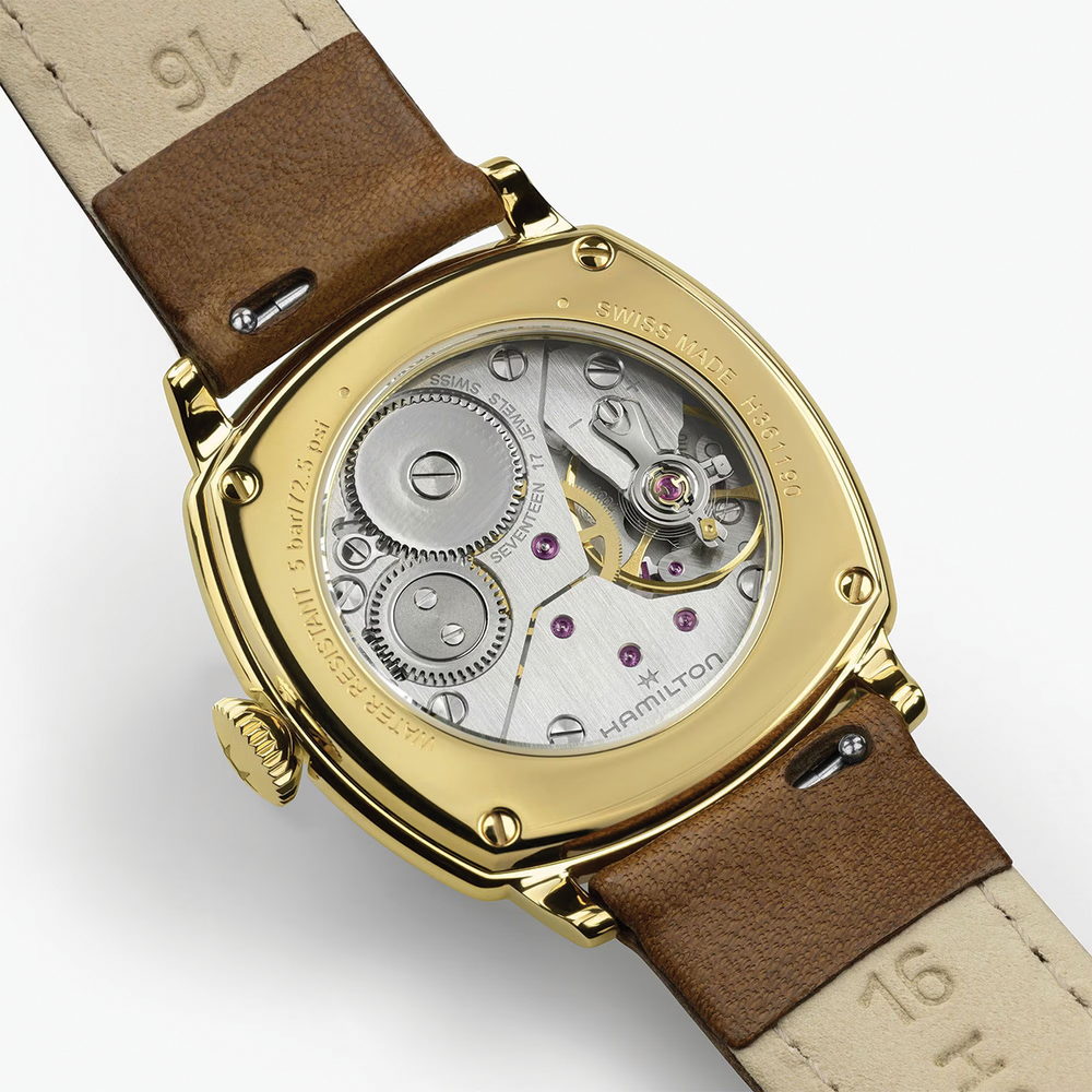 Gold tone case back of cushion style Hamilton watch showing exposed movement and brown leather strap.