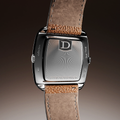 Back view of a Dennison ALD Dual Time watch with a D logo on the case back and a brown leather strap.