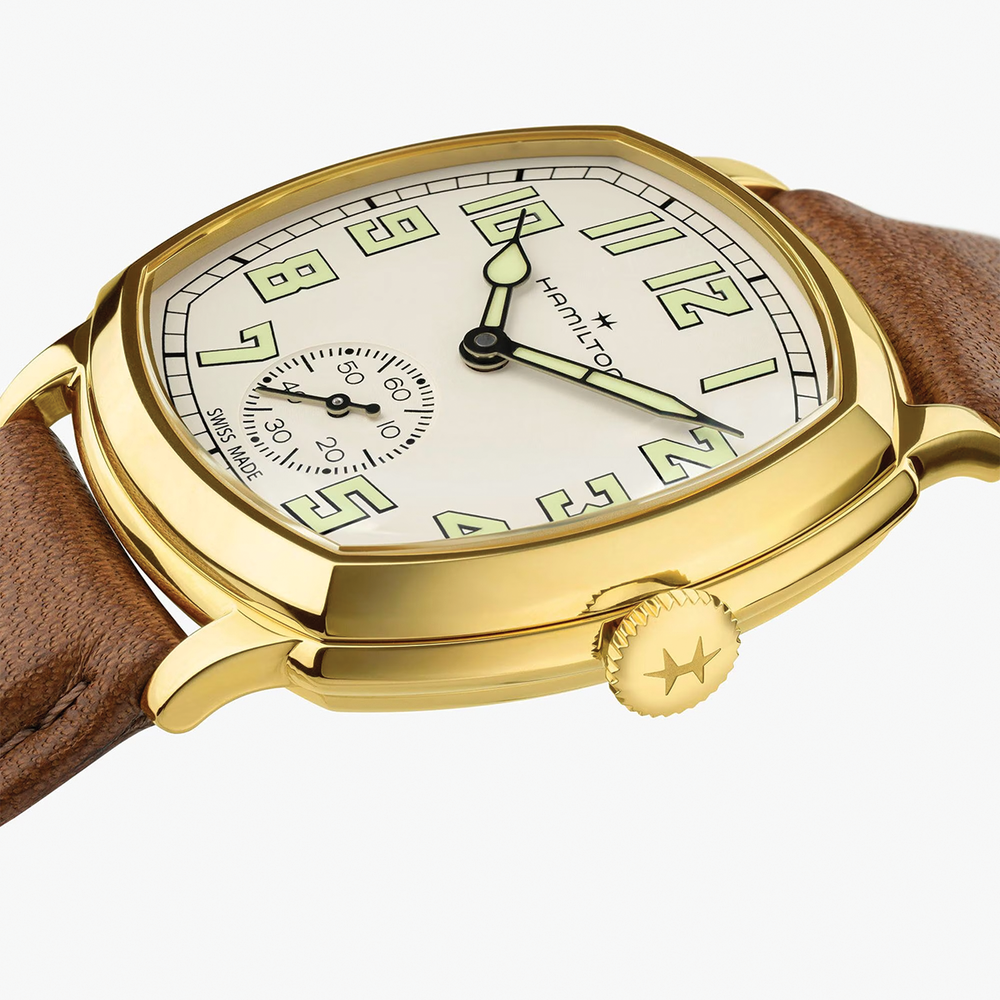 Angled close-up of gold-tone cushion watch with brown leather strap and crown detail.