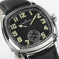 Angled view of American Classic Cushion Mechanical 34mm watch with black dial luminous numerals and polished steel case on a black leather strap.