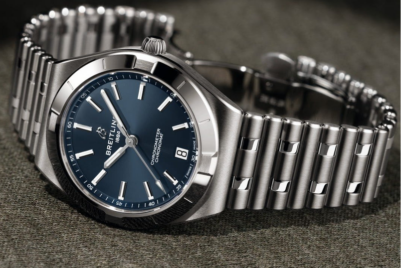 Silver Breitling watch with blue dial on a dark textured surface
