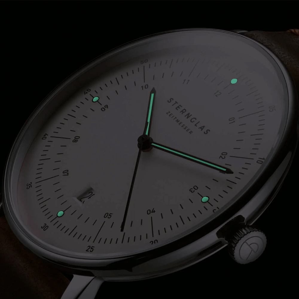 Hamburg watch dial in low light with glowing teal luminescent hands and markers