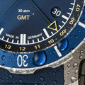 Detail of Seebataillon GMT dial with yellow GMT triangle marker and 30 atm GMT text blue bezel and water droplets.